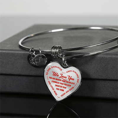 TO OUR DAUGHTER, WE LOVE YOU - SILVER OR GOLD FINISHED HEART SHAPED BANGLE BRACELET (RED ON TRANSPARENT)
